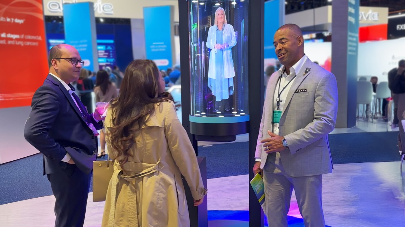 Physicians talking beside a life-size AI host in a HoloTube HalfPipe on a medical congress floor